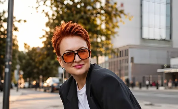 Валентина Сухарева в чёрном костюме и оранжевых очках улыбается на вечерней улице
